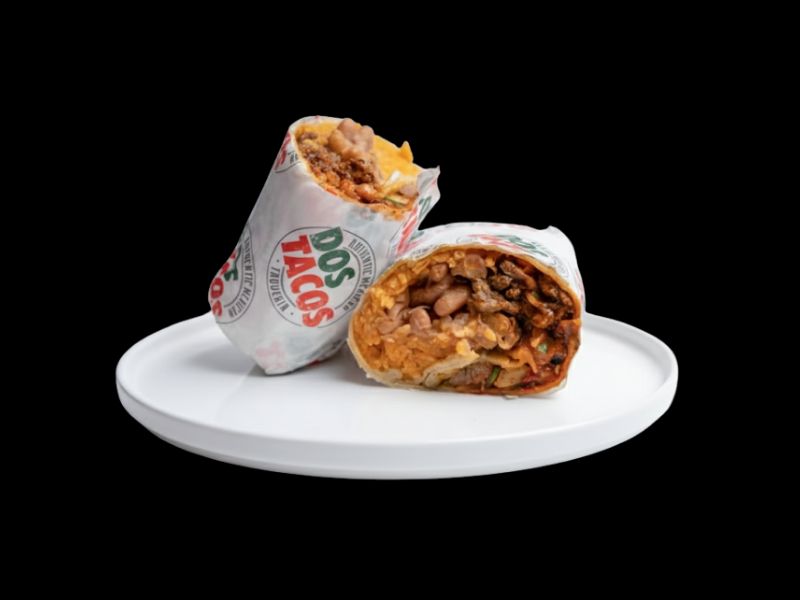 Two halves of a large Mexican burrito wrapped in Dos Tacos branded paper, showing the inside filling of rice, pinto beans, and shredded meat on a white plate.