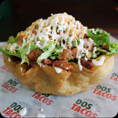 A crispy, edible flour tortilla bowl filled with a taco salad mix of seasoned meat, shredded lettuce, cheese, and sour cream